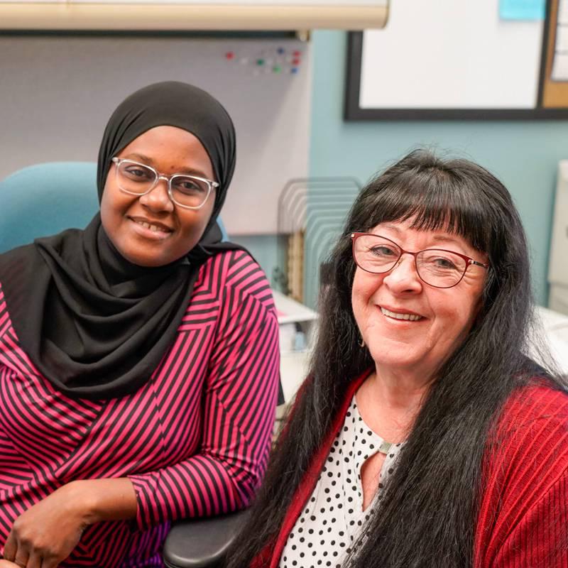 An accounting student and professor sit at a desk smiling